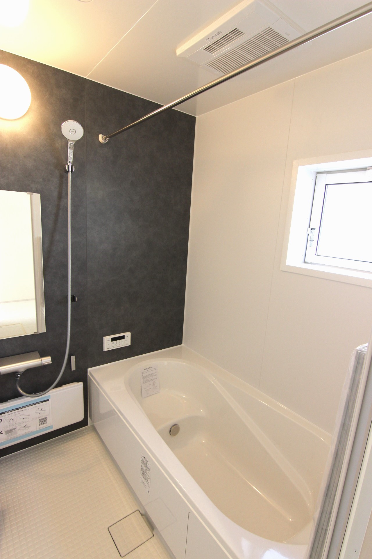 【1号棟:浴室】　白を基調とし、モルティオダークの壁を一面に敷いたシックな雰囲気の浴室。浴室暖房換気乾燥機付。浴槽は温かさが続くサーモバスS構造。　※浴室・浴槽の仕様は全棟共通です